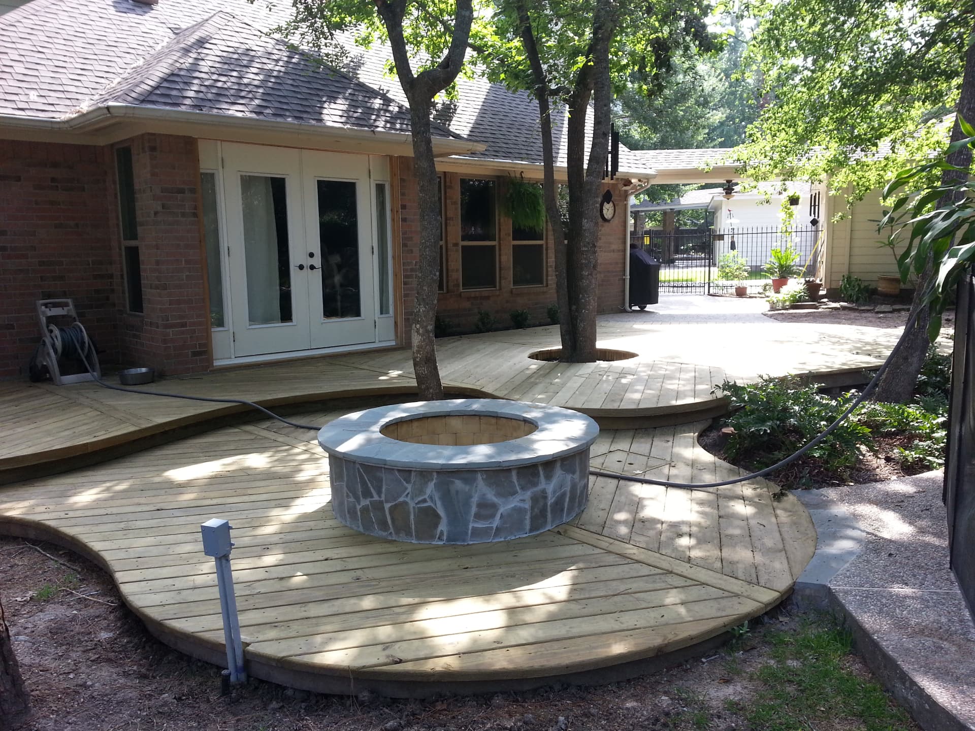 Stone-clad fire pit built into a curved wood deck beside a brick home