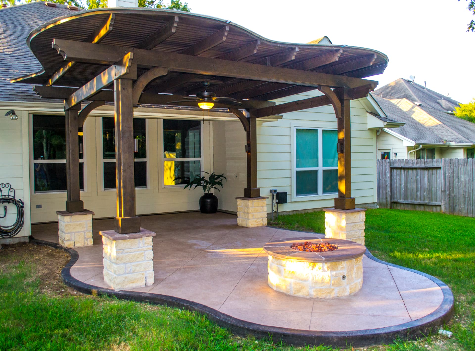 Traditional pergola over a stained concrete patio with a limestone gas fire pit at dusk