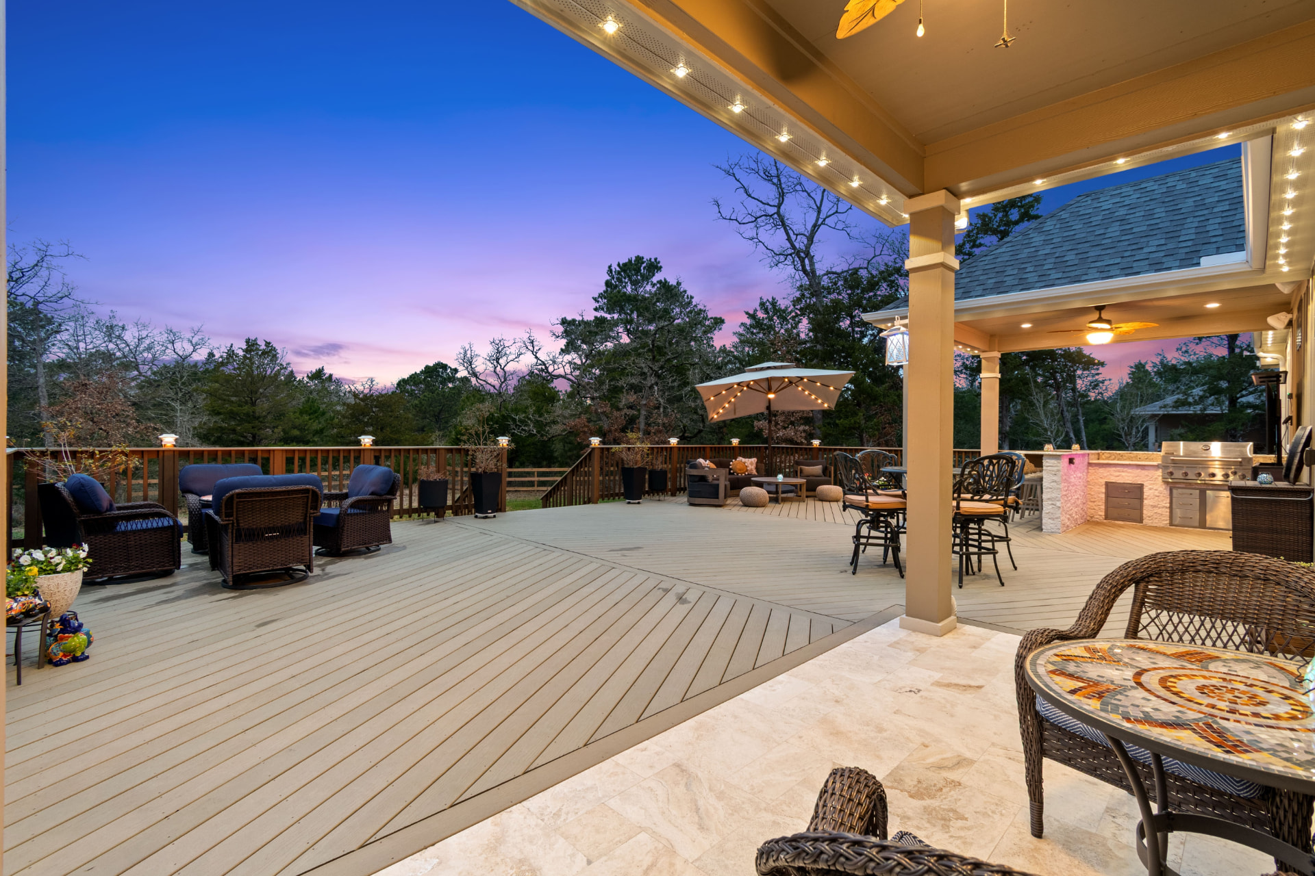 Expansive elevated composite deck with outdoor kitchen and covered dining at dusk