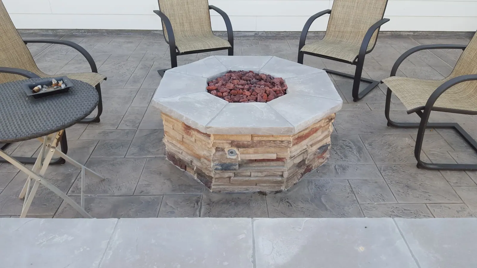 Octagonal stacked stone natural gas fire pit with lava rock on a stamped concrete patio