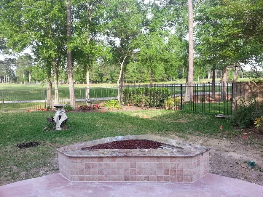 Hexagonal tiled gas fire pit on a patio overlooking a wooded backyard