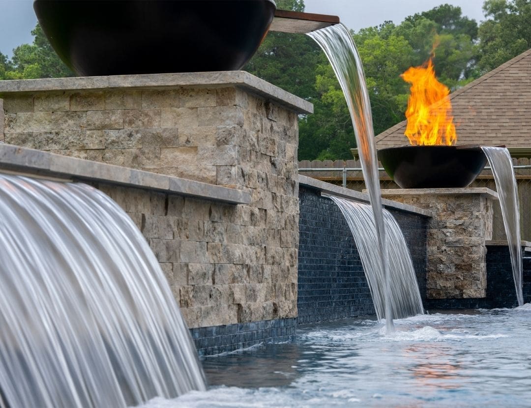 Close-up of fire and water bowl feature spilling into custom pool with stacked stone wall