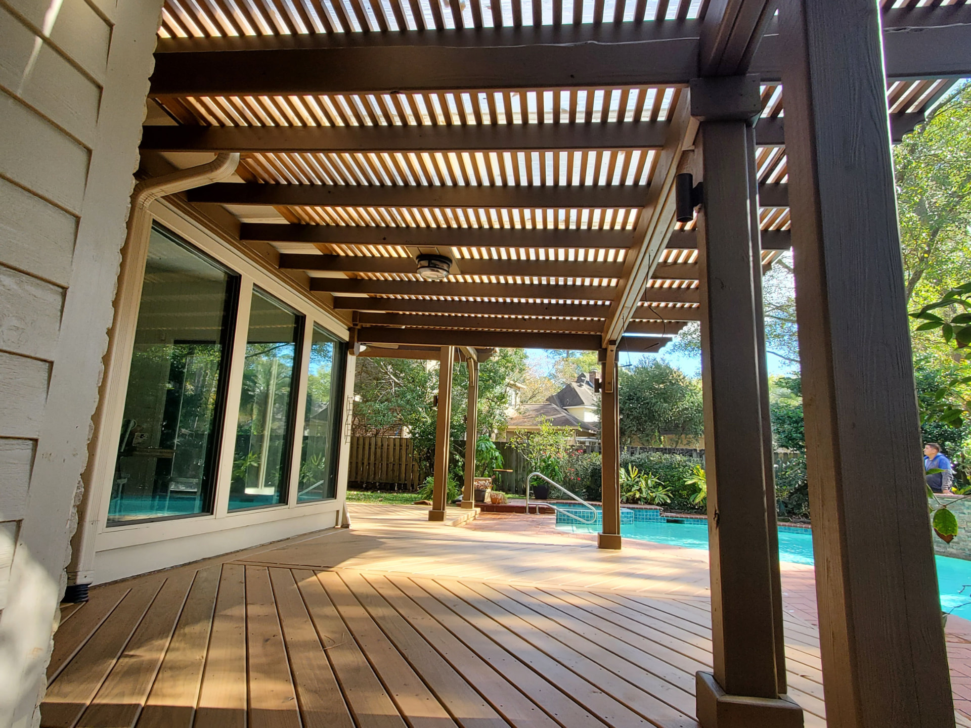 Attached cedar pergola with slatted roof over wood deck alongside pool