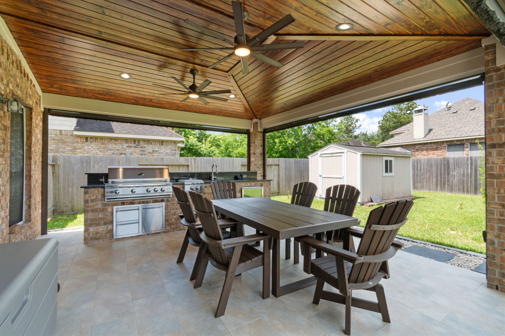 Covered outdoor kitchen with grill, dining table and vaulted wood ceiling