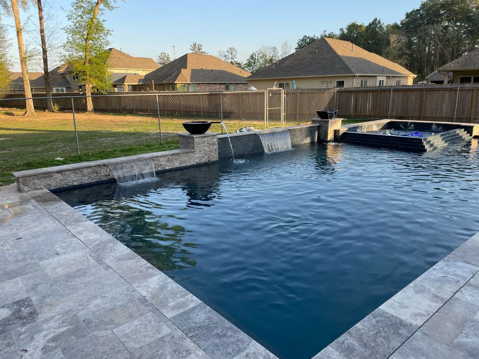 Modern geometric pool with sheer-descent waterfalls, fire bowls and raised spa