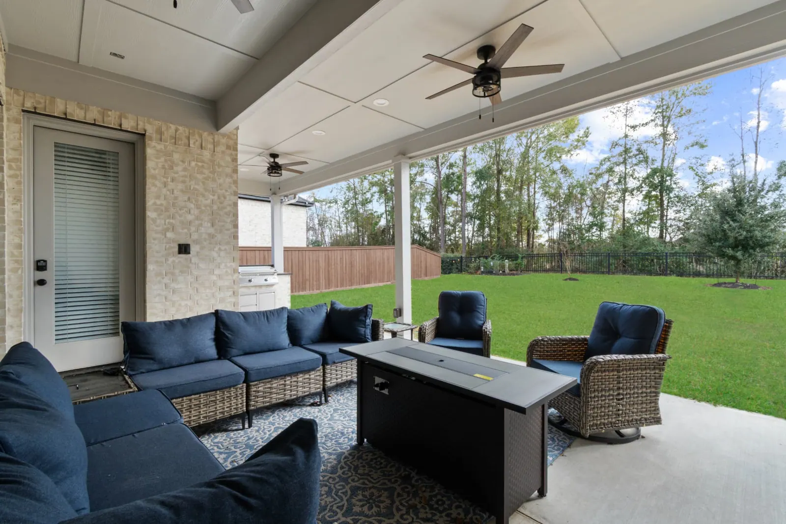 Covered patio with navy sectional and fire table overlooking backyard