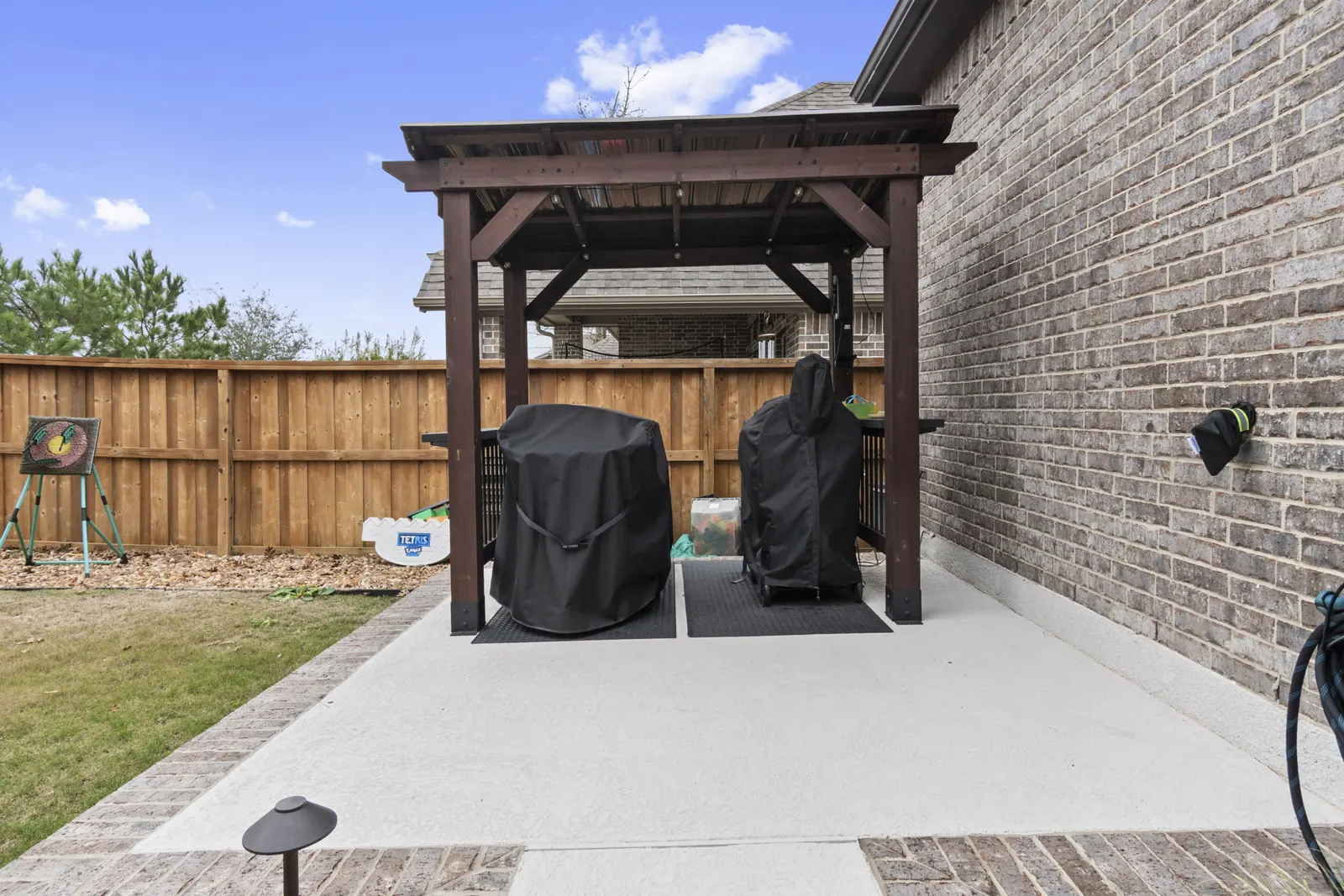 Compact stained cedar pergola with metal roof over side-yard grill station