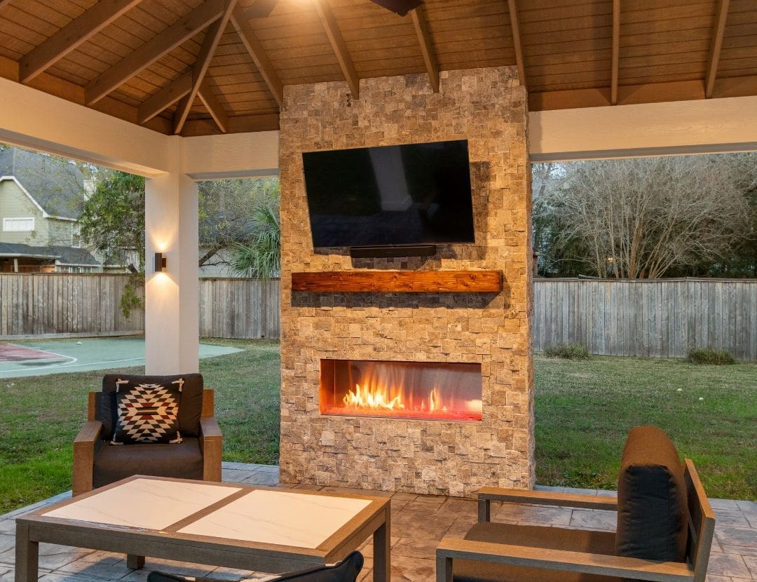 Close-up of stacked-stone outdoor fireplace with reclaimed wood mantel and mounted TV