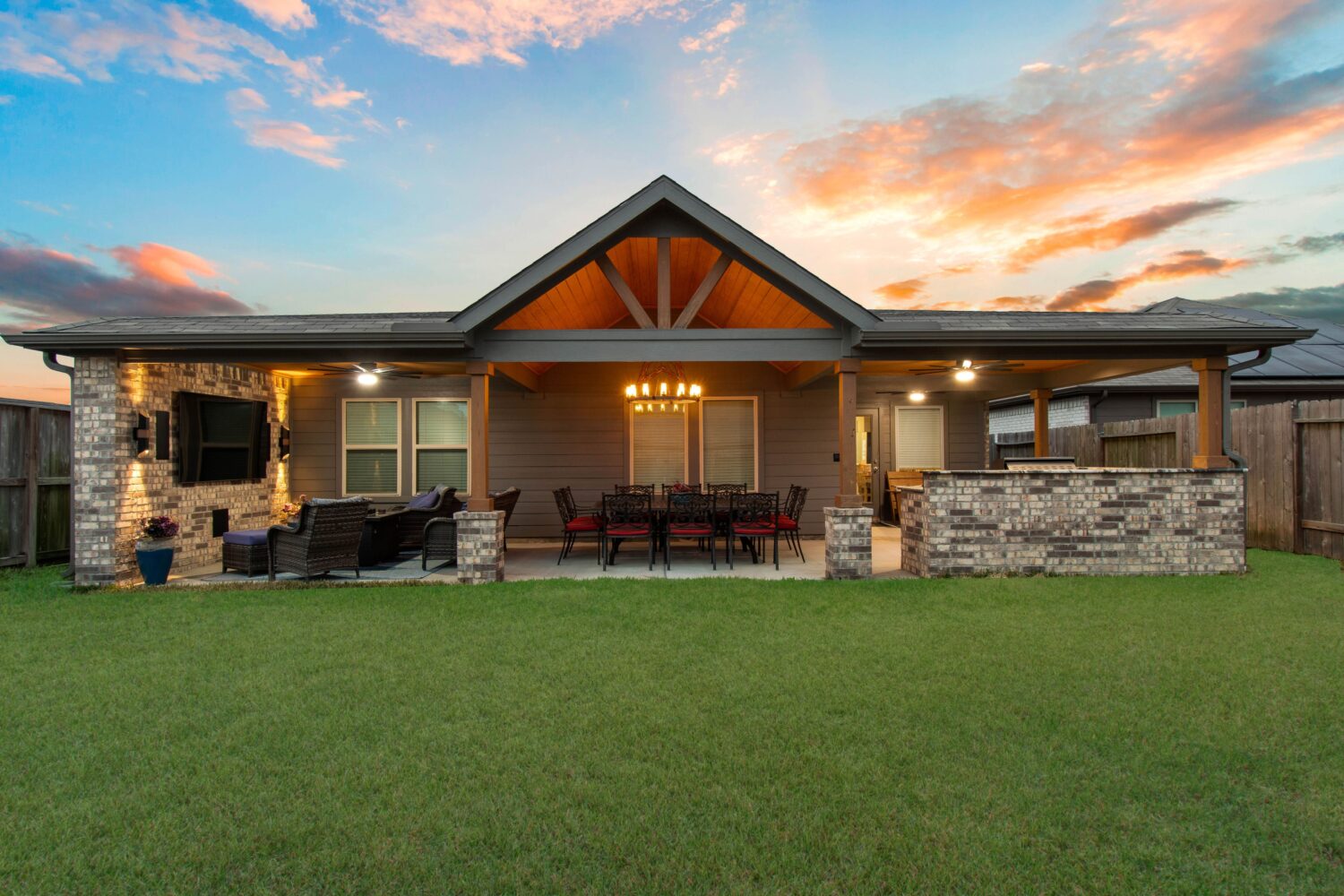 Attached gabled patio cover with cedar trusses, chandelier and outdoor kitchen at sunset