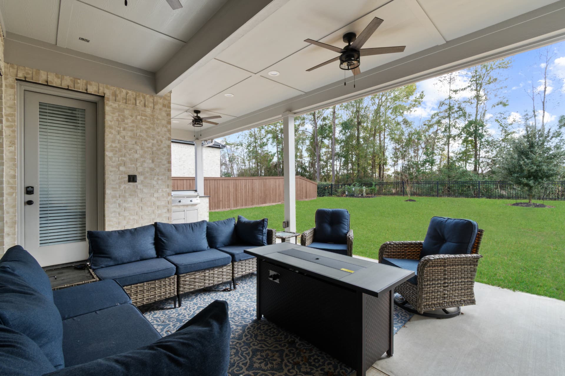 Covered patio with navy sectional and fire table overlooking backyard