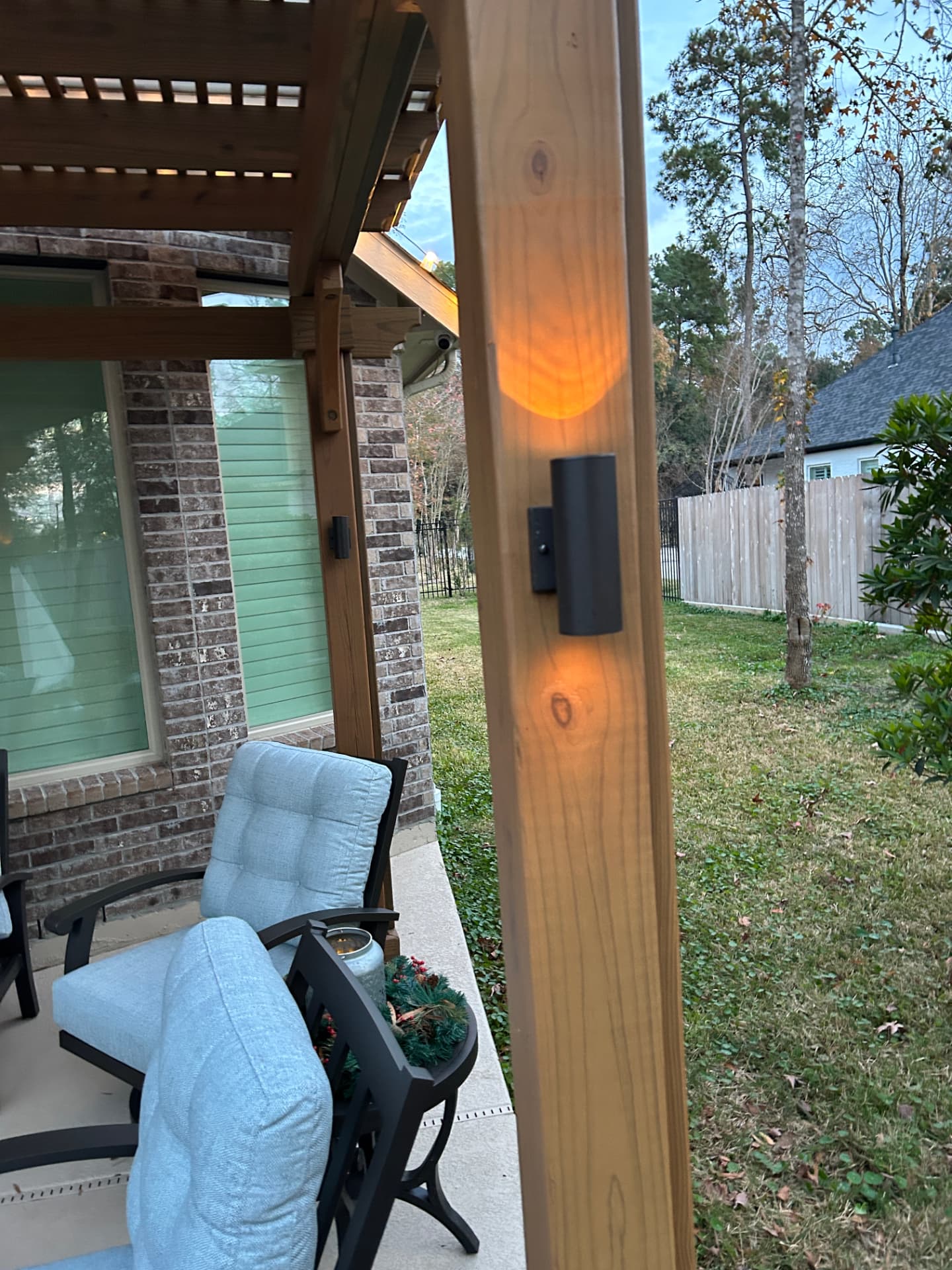 Wooden pergola post with sconce lighting, brick columns, and cushioned seating