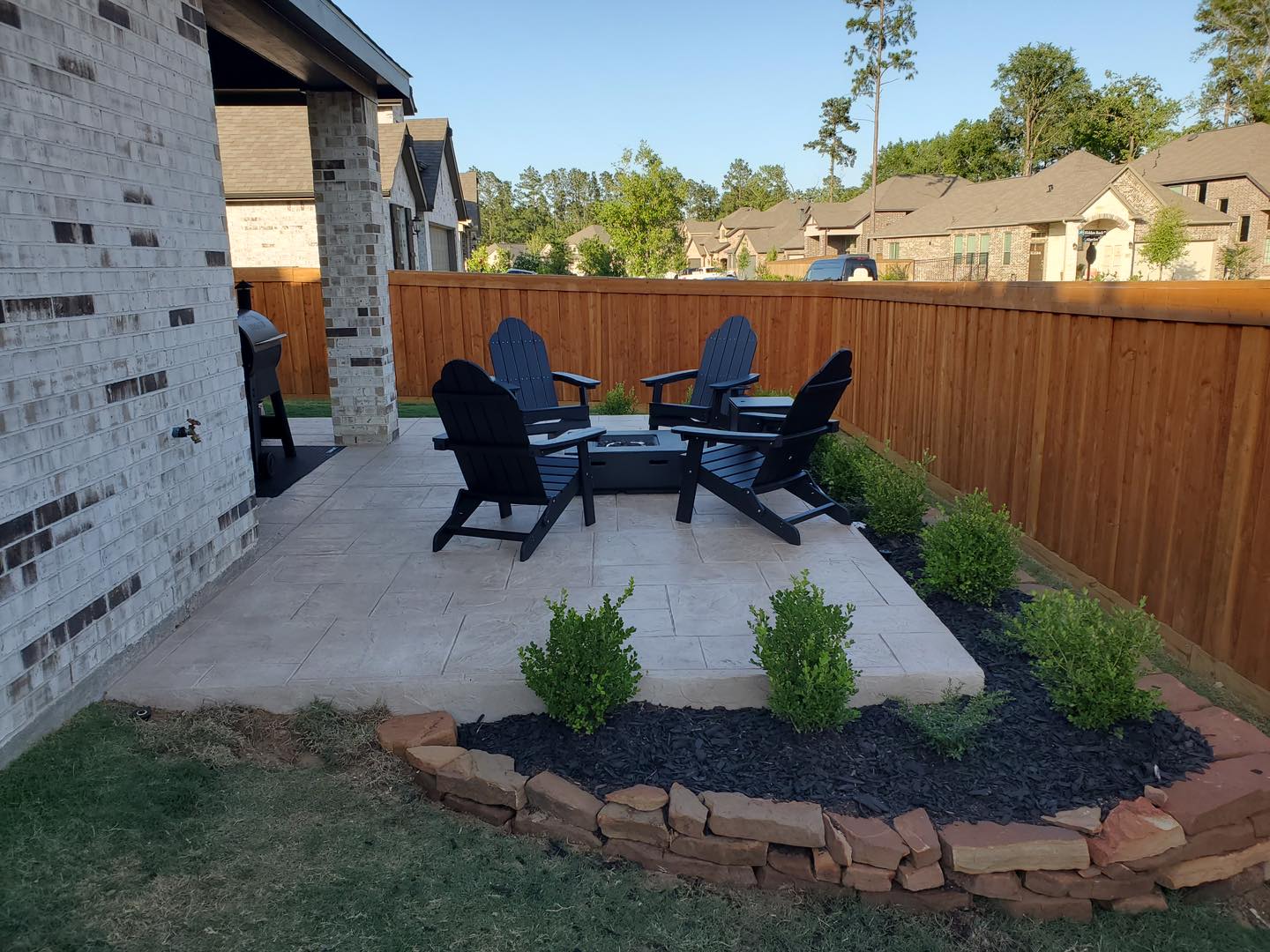 Stamped concrete patio with Adirondack chairs around fire table and landscaped border
