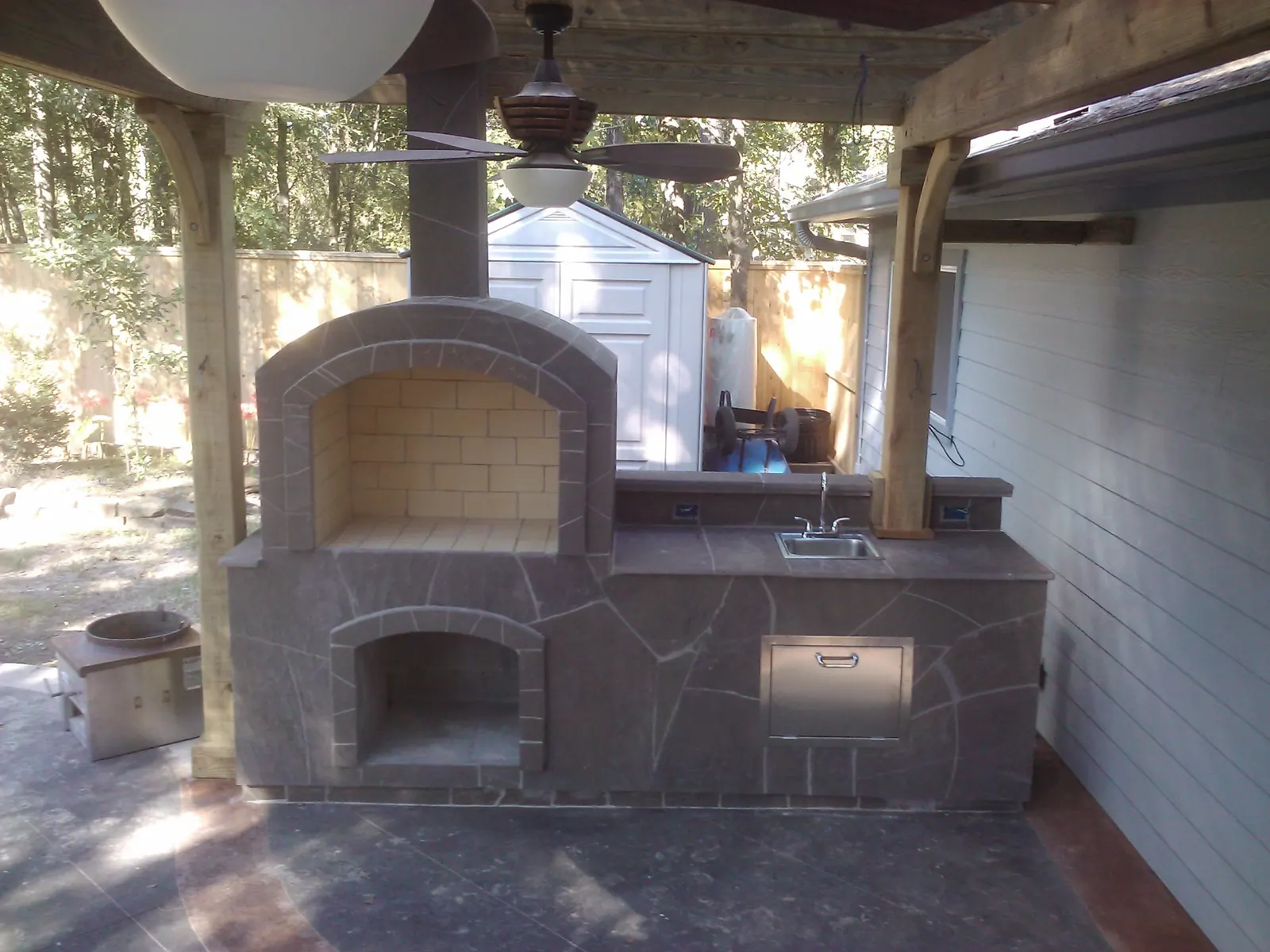 Flagstone outdoor kitchen with built-in fireplace, sink, and pergola cover