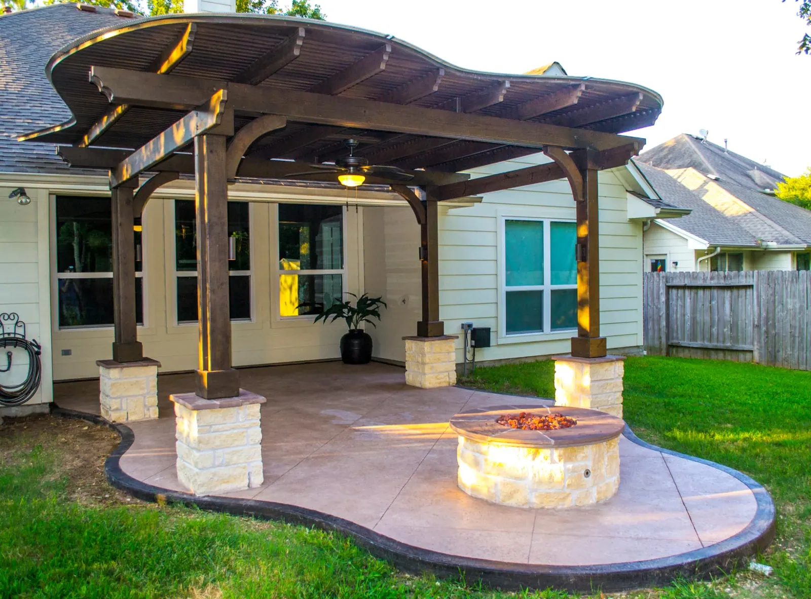 Traditional pergola over a stained concrete patio with a limestone gas fire pit at dusk