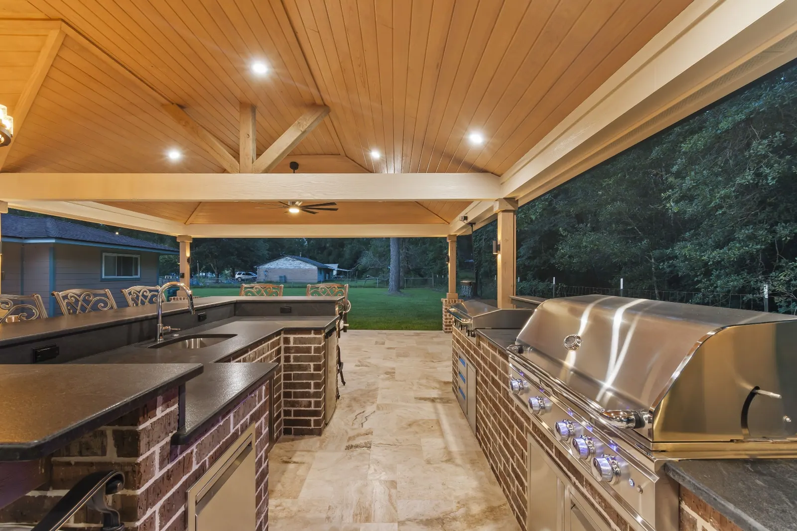 Full outdoor kitchen with grill, sink, and bar seating at dusk