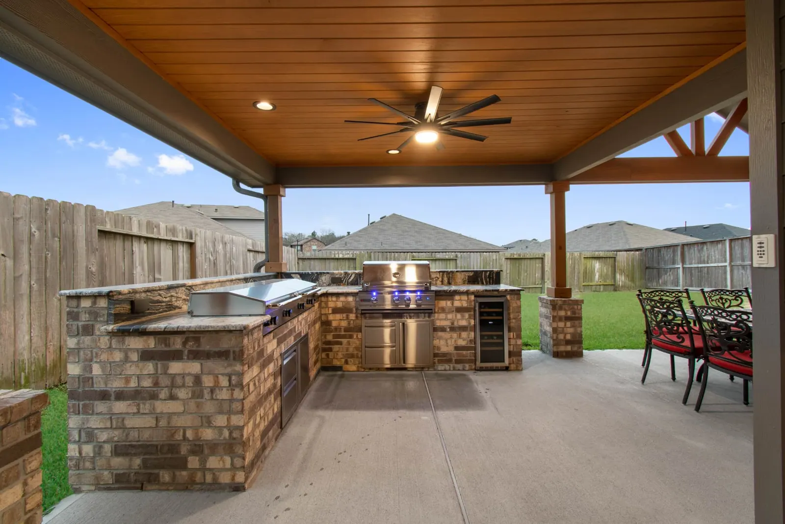 Brick outdoor kitchen with griddle, grill and wine cooler under wood-plank patio cover