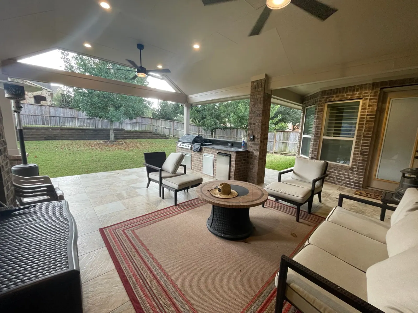 Covered patio with vaulted ceiling, ceiling fans, brick outdoor kitchen and fire pit lounge