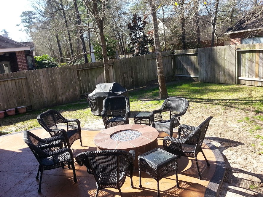 Round gas fire pit with fire glass on a stamped concrete patio with wicker seating