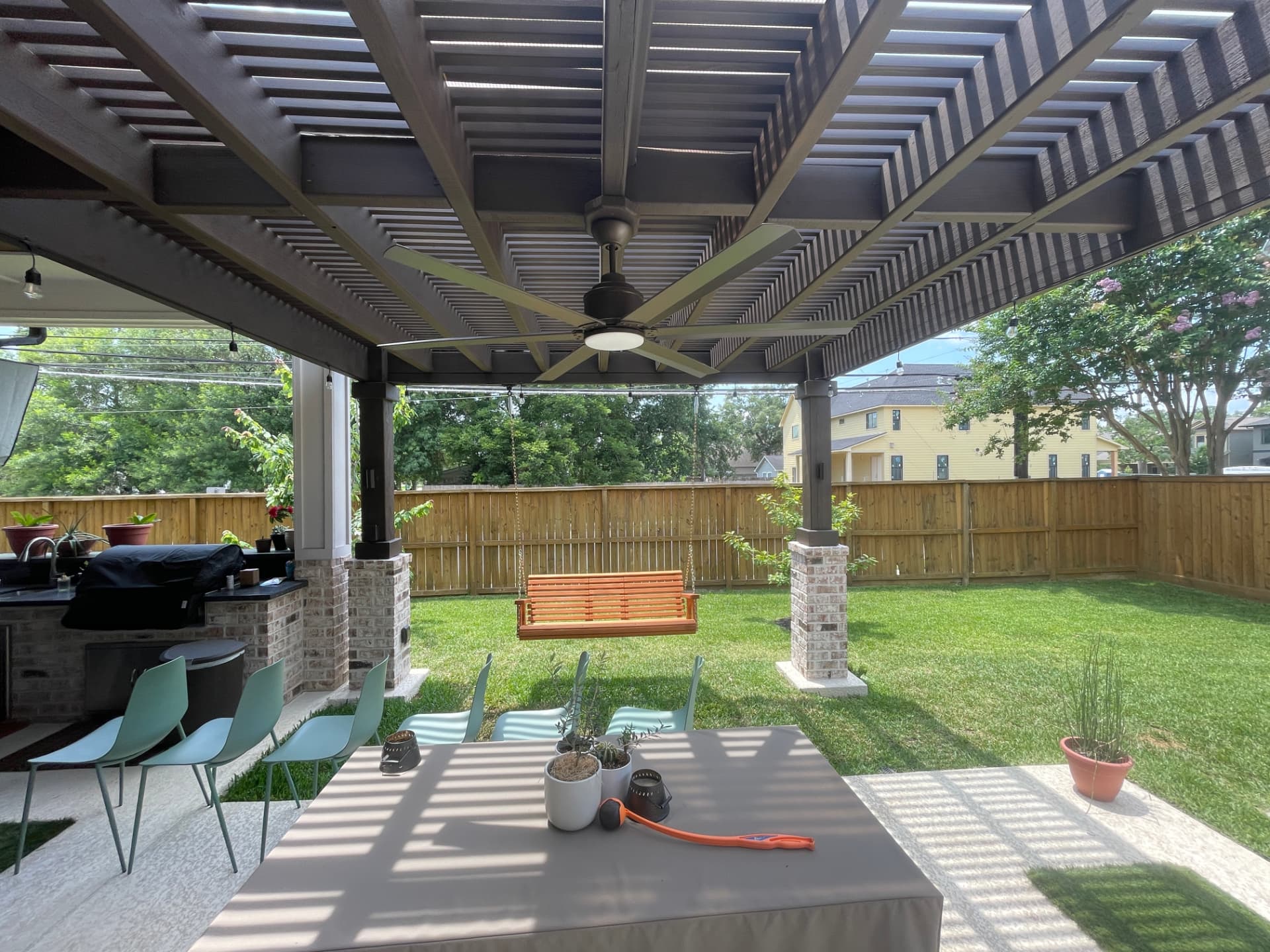 Underside of modern louvered pergola with ceiling fan and string lights