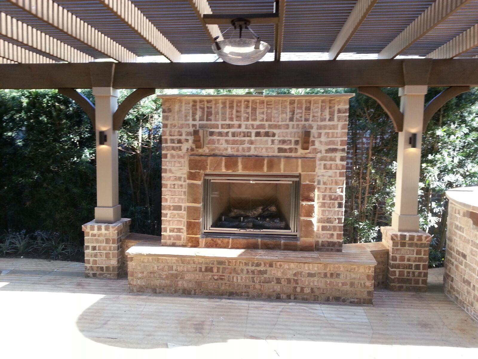 Brick outdoor fireplace with hearth bench beneath a pergola