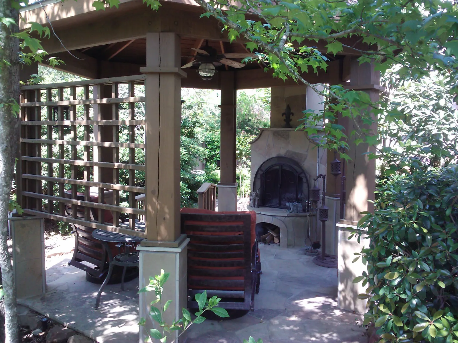 Stone outdoor fireplace under a cedar gazebo on a flagstone patio