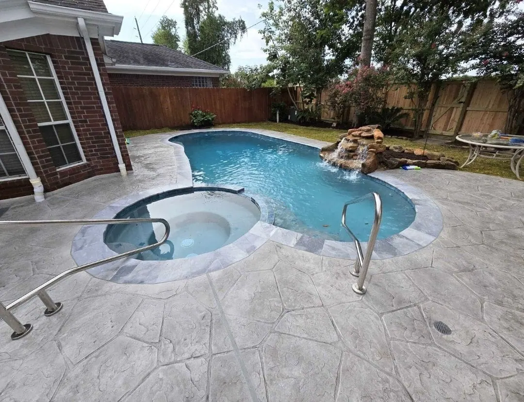 Freeform pool with attached spa, rock waterfall and stamped concrete decking