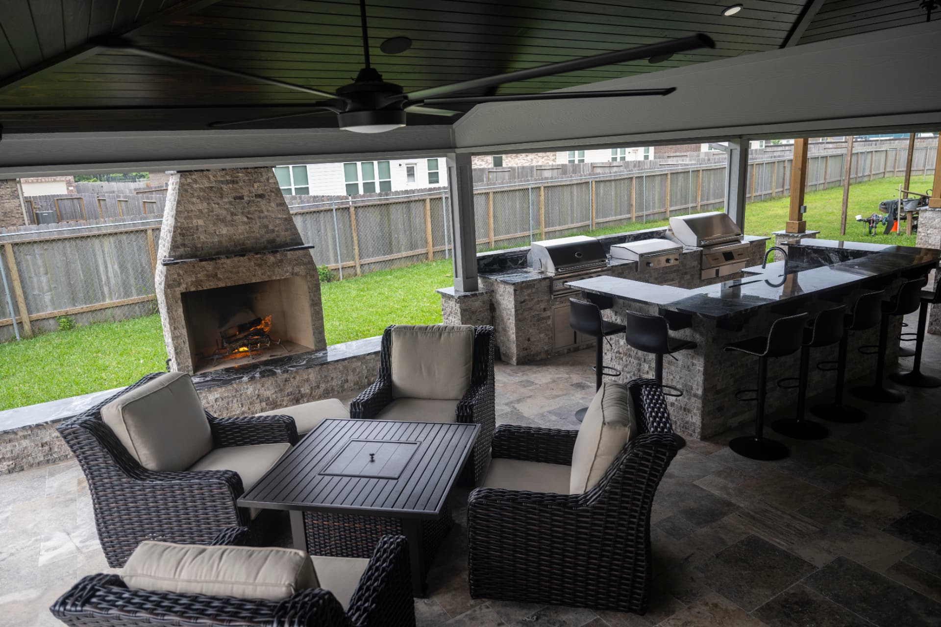 Covered patio with stone fireplace, lounge seating and long bar-height outdoor kitchen