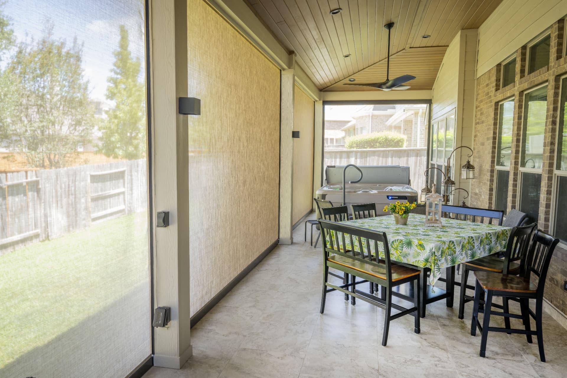 Covered patio with motorized privacy screens down alongside hot tub and dining area