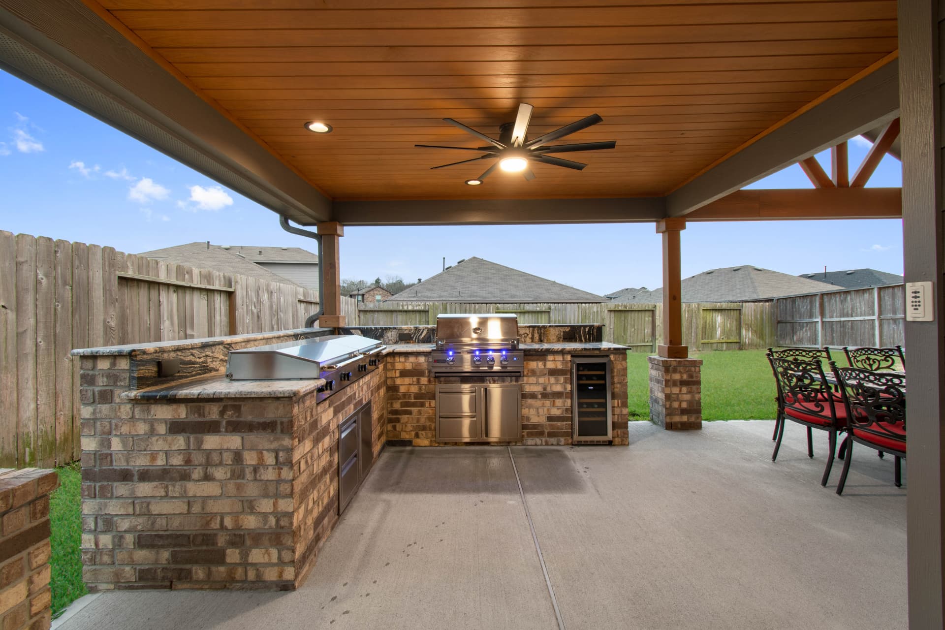 Brick outdoor kitchen with griddle, grill and wine cooler under wood-plank patio cover