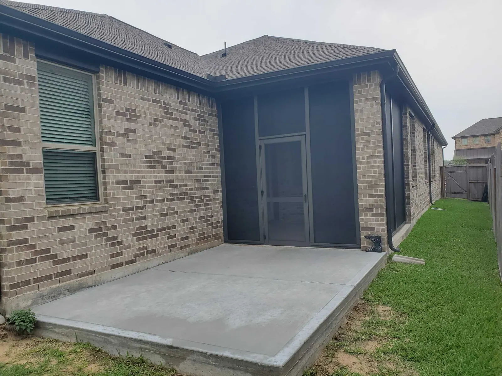 Screened porch enclosure with dark mesh panels and screen door on a brick home