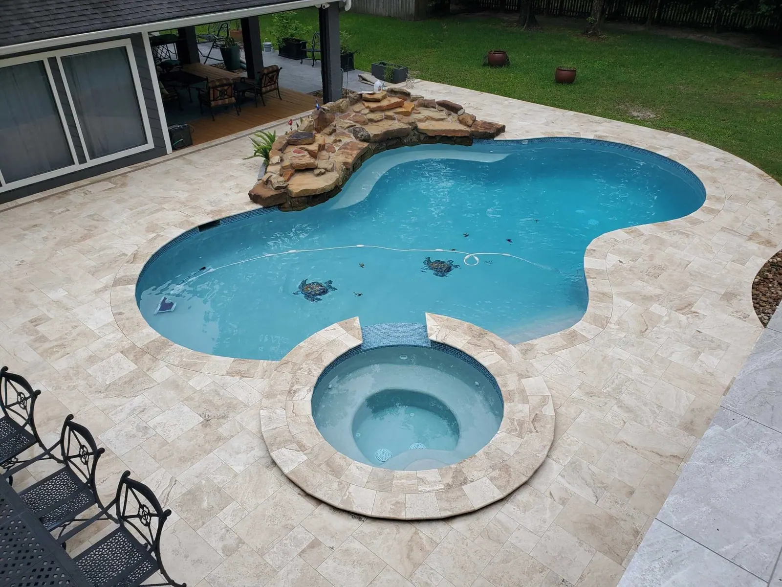 Freeform pool with attached round spa, rock waterfall and travertine deck