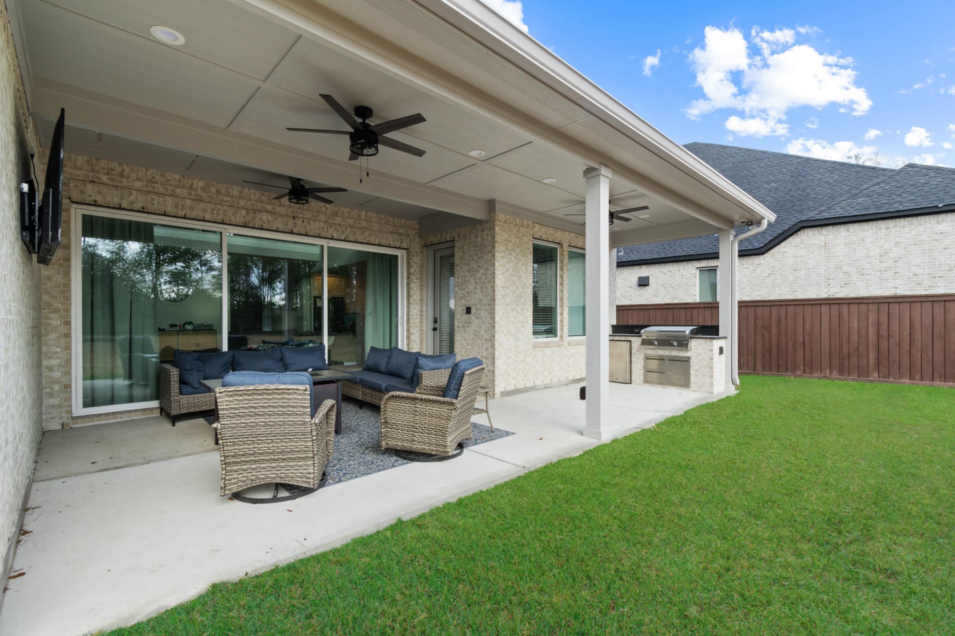 Covered patio with navy wicker lounge seating, outdoor kitchen and ceiling fans