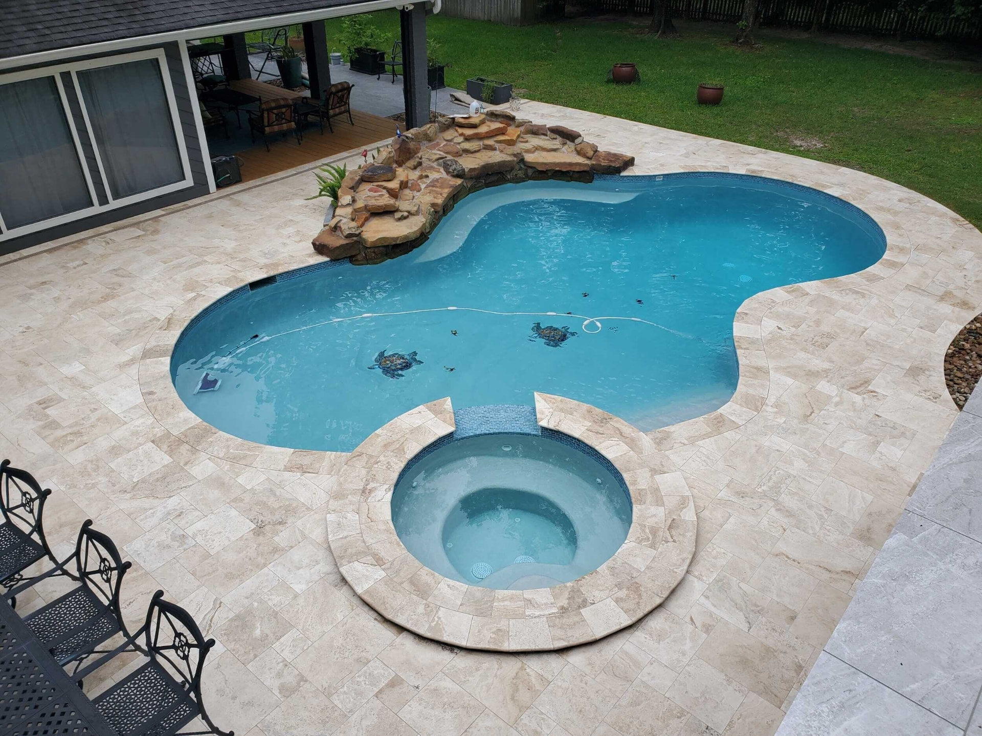 Freeform pool with attached round spa, rock waterfall and travertine deck