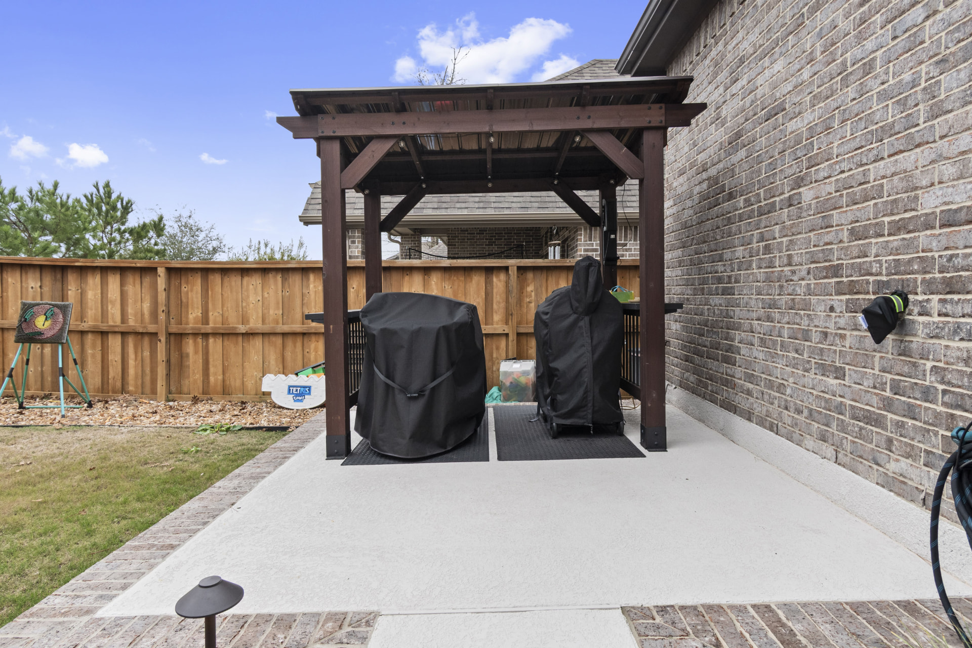 Compact stained cedar pergola with metal roof over side-yard grill station