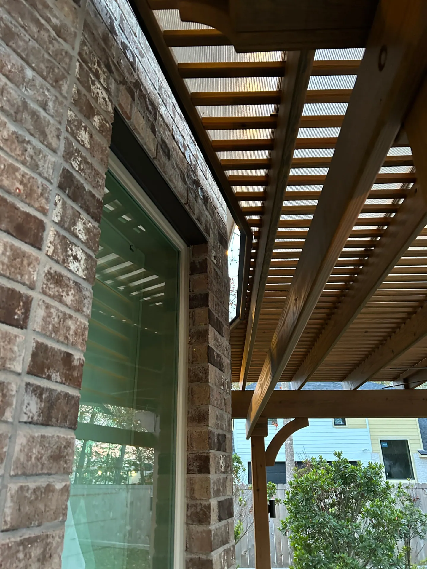 Wooden pergola with brick columns attached to home with polycarbonate roof panels