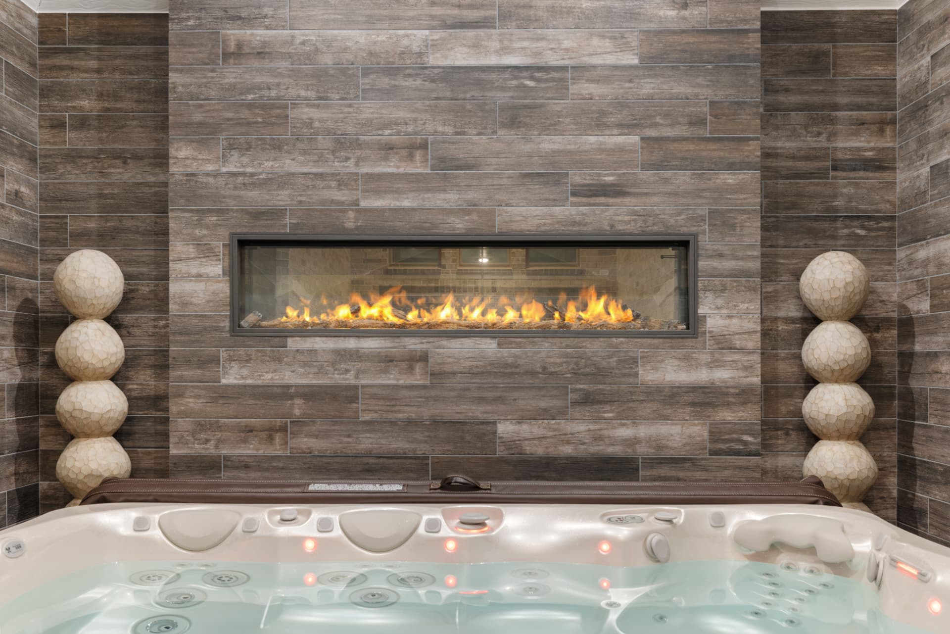 Linear gas fireplace on wood-plank tile wall behind luxury hot tub