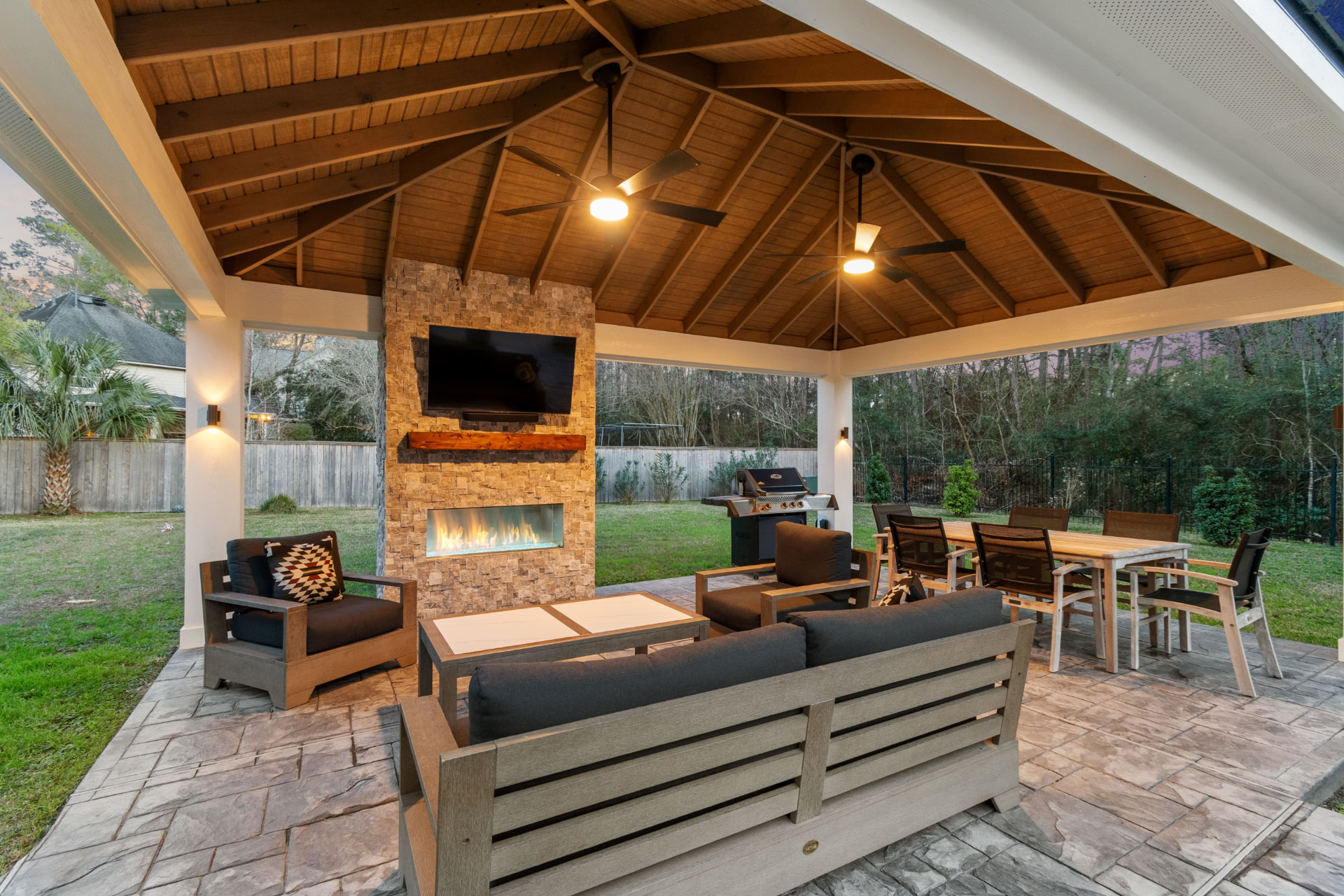 Freestanding pavilion with stacked-stone linear gas fireplace, TV and vaulted cedar ceiling