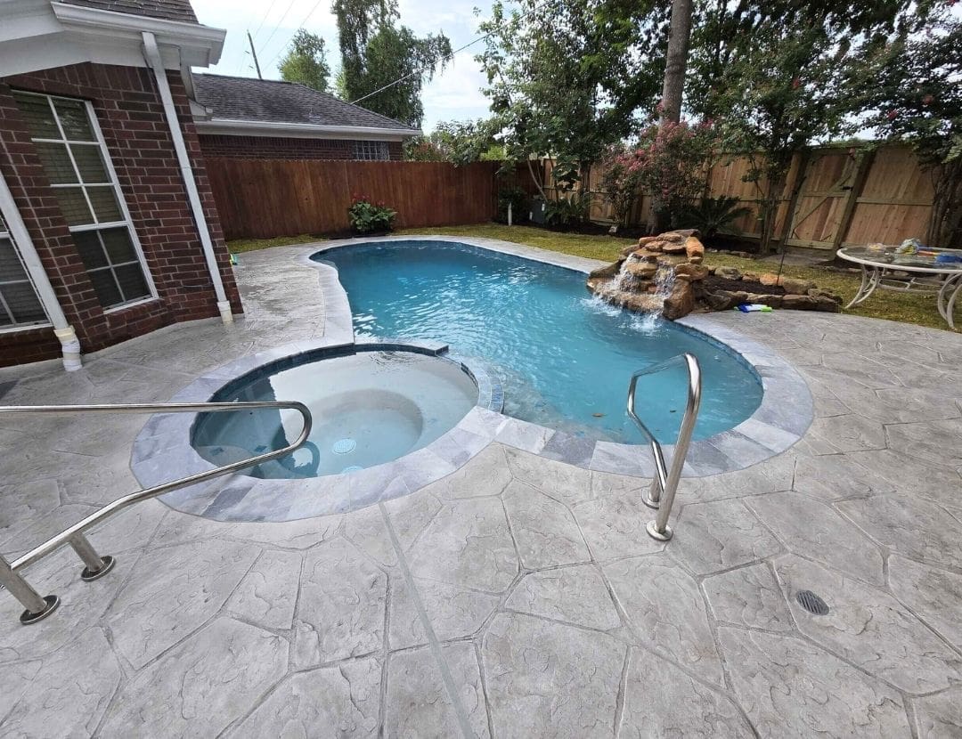 Freeform pool with attached spa, rock waterfall and stamped concrete decking