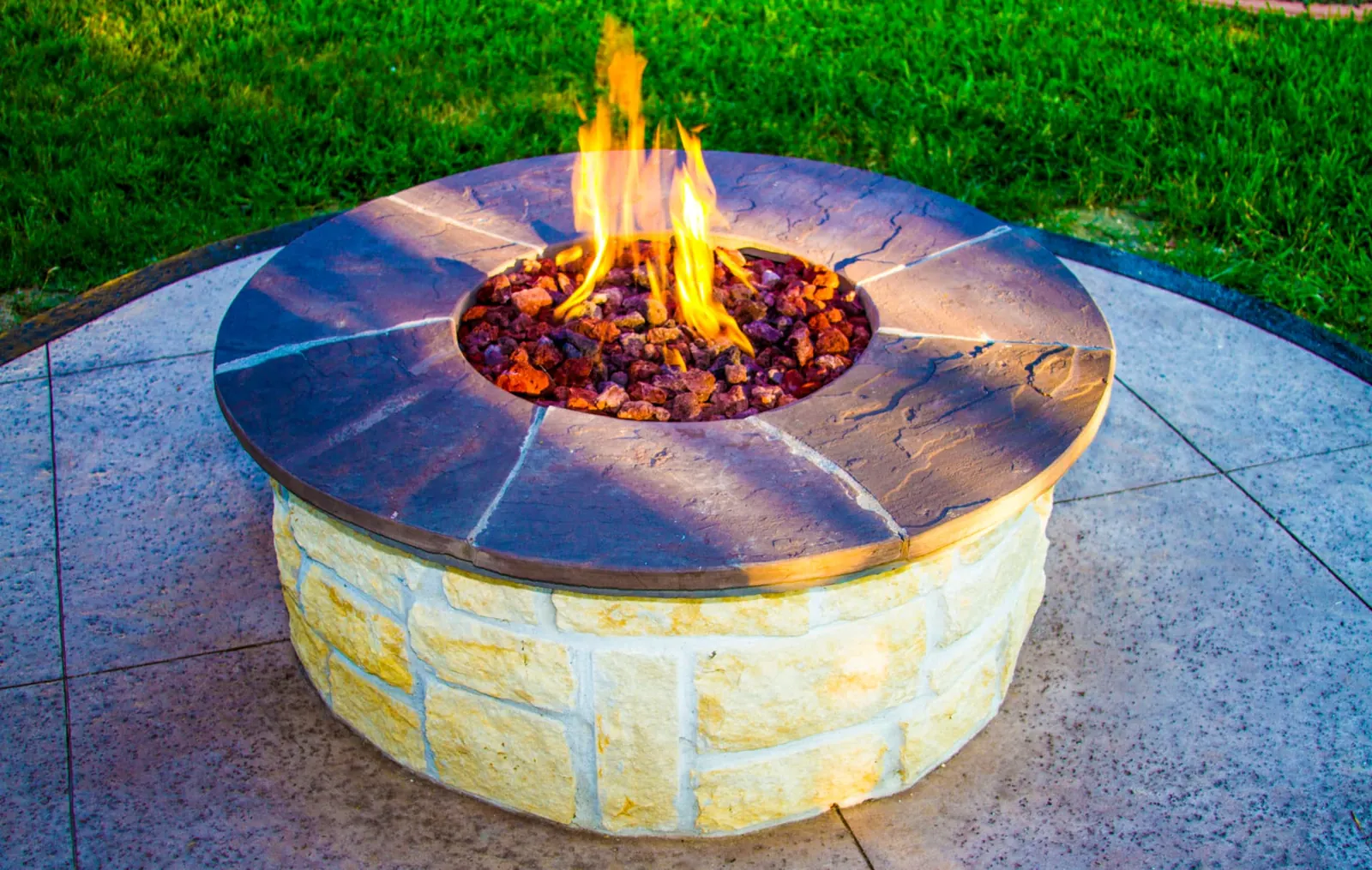 Round limestone fire pit with flagstone cap and natural gas flame