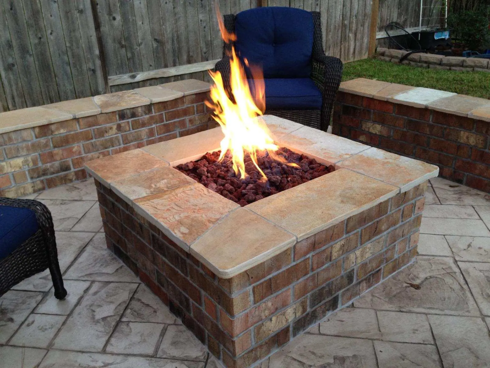 Brick natural gas fire pit with lava rock burning beside cushioned seating
