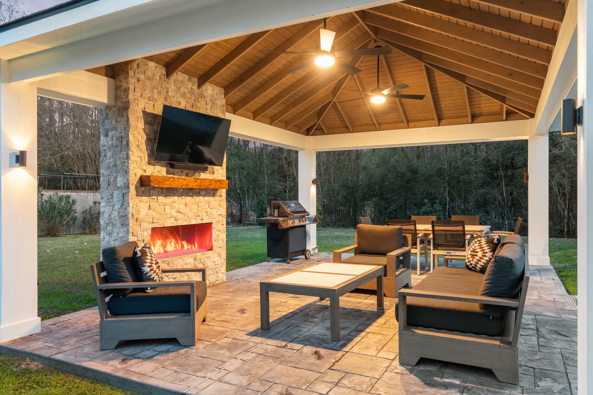 Twilight view of freestanding pavilion with lit stone fireplace and outdoor kitchen